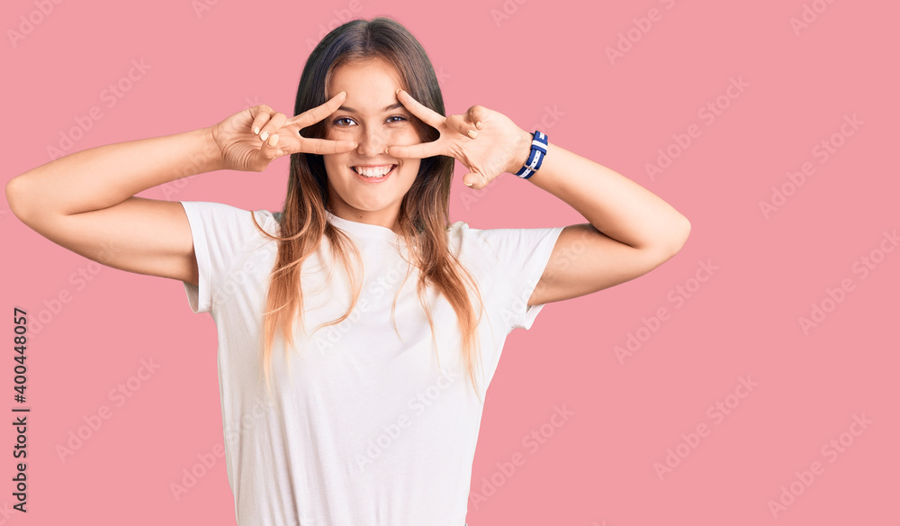 Beautiful caucasian woman wearing casual white tshirt doing peace symbol with fingers over face, smiling cheerful showing victory Beautiful caucasian woman wearing casual white tshirt doing peace symbol with fingers over face, smiling cheerful showing victory