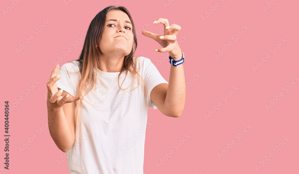 Beautiful caucasian woman wearing casual white tshirt shouting frustrated with rage, hands trying to strangle, yelling mad Beautiful caucasian woman wearing casual white tshirt shouting frustrated with rage, hands trying to strangle, yelling mad
