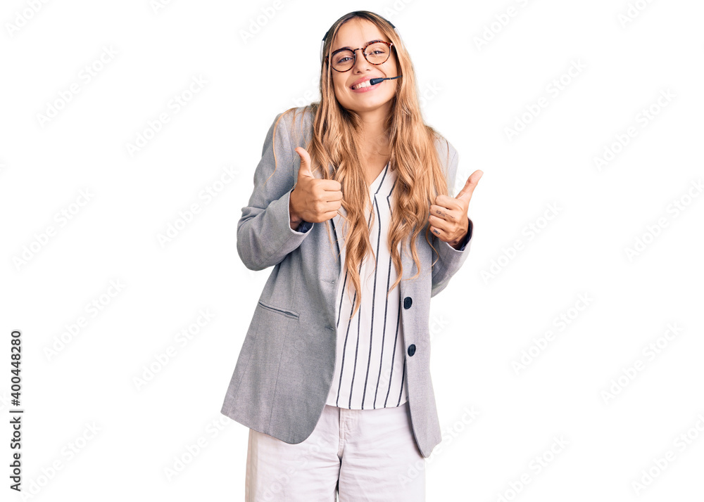 Obraz premium Young beautiful blonde woman wearing call center agent headset success sign doing positive gesture with hand, thumbs up smiling and happy. cheerful expression and winner gesture.