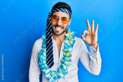 Young hispanic businessman wearing party funny style with tie on head smiling positive doing ok sign with hand and fingers. successful expression.