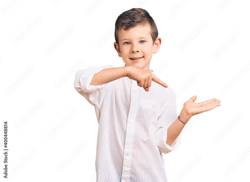 Cute blond kid wearing elegant shirt amazed and smiling to the camera while presenting with hand and pointing with finger. Cute blond kid wearing elegant shirt amazed and smiling to the camera while presenting with hand and pointing with finger.