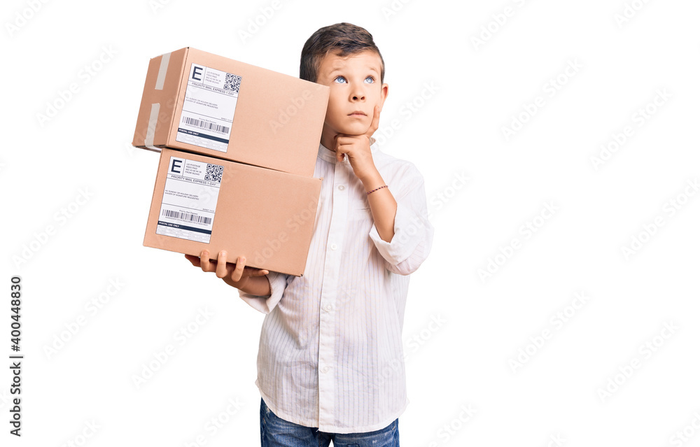 Cute blond kid holding delivery package serious face thinking about question with hand on chin, thoughtful about confusing idea Cute blond kid holding delivery package serious face thinking about question with hand on chin, thoughtful about confusing idea