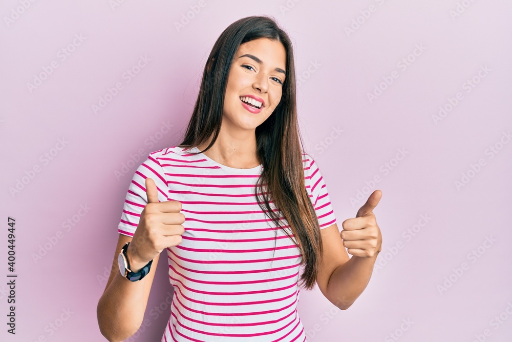 Young brunette woman wearing casual clothes over pink background success sign doing positive gesture with hand, thumbs up smiling and happy. cheerful expression and winner gesture. Young brunette woman wearing casual clothes over pink background success sign doing positive gesture with hand, thumbs up smiling and happy. cheerful expression and winner gesture.