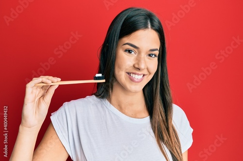 Fototapeta Naklejka Na Ścianę i Meble -  Young brunette woman holding toothbrush with toothpaste looking positive and happy standing and smiling with a confident smile showing teeth