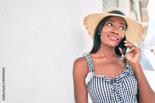 Young african american woman on vacation talking on the smartphone leaning on the wall at street of city