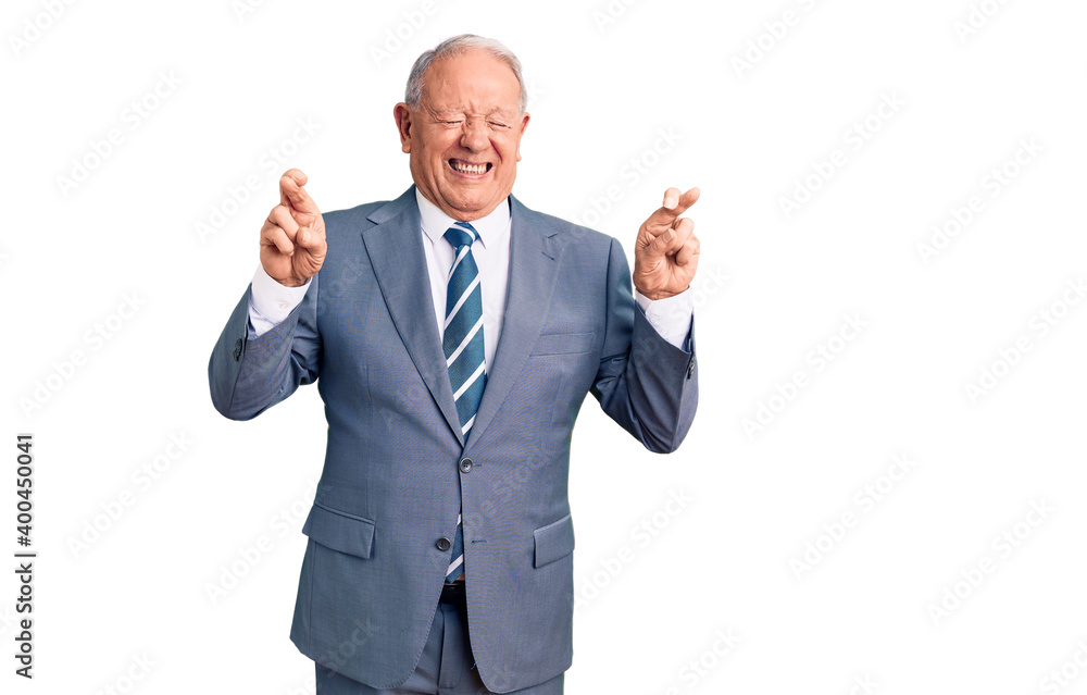 Senior handsome grey-haired man wearing elegant suit gesturing finger crossed smiling with hope and eyes closed. luck and superstitious concept. Senior handsome grey-haired man wearing elegant suit gesturing finger crossed smiling with hope and eyes closed. luck and superstitious concept.