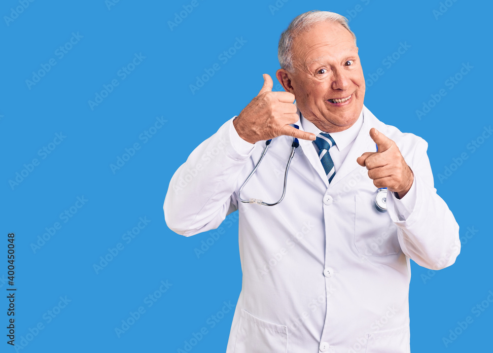 Senior handsome grey-haired man wearing doctor coat and stethoscope smiling doing talking on the telephone gesture and pointing to you. call me. Senior handsome grey-haired man wearing doctor coat and stethoscope smiling doing talking on the telephone gesture and pointing to you. call me.