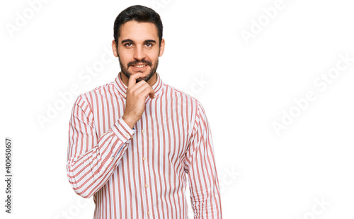 Young hispanic man wearing business shirt looking confident at the camera with smile with crossed arms and hand raised on chin. thinking positive.