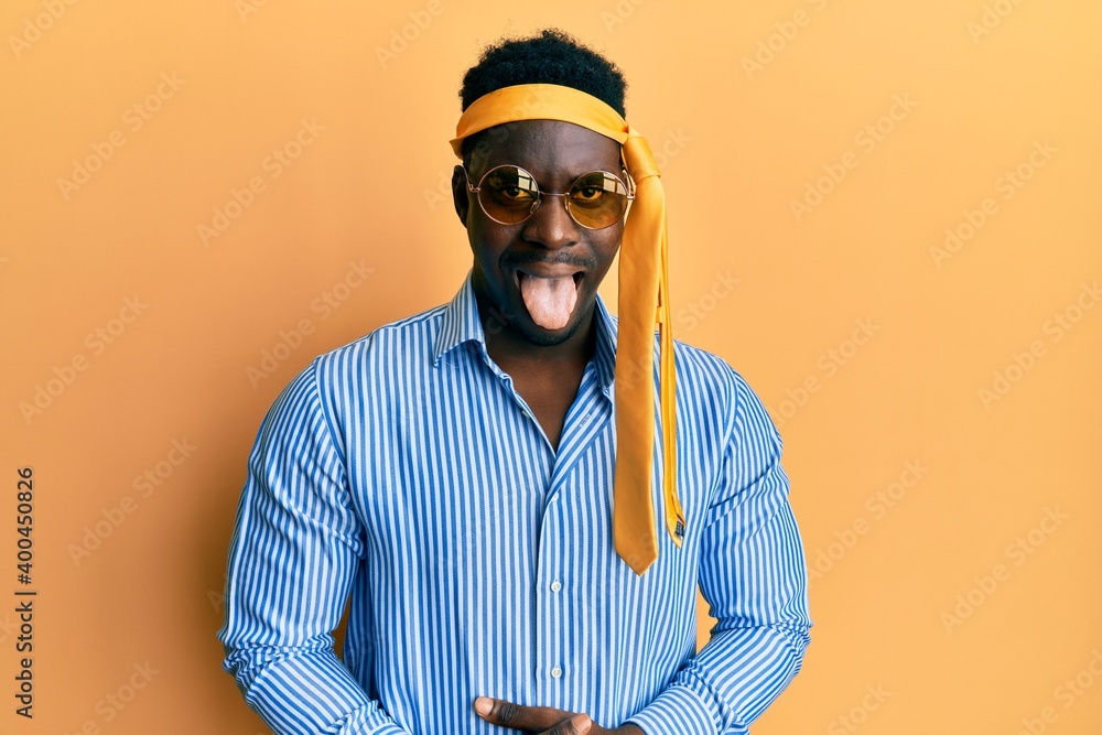 Handsome black man drunk wearing tie over head and sunglasses sticking tongue out happy with funny expression. emotion concept. Handsome black man drunk wearing tie over head and sunglasses sticking tongue out happy with funny expression. emotion concept.