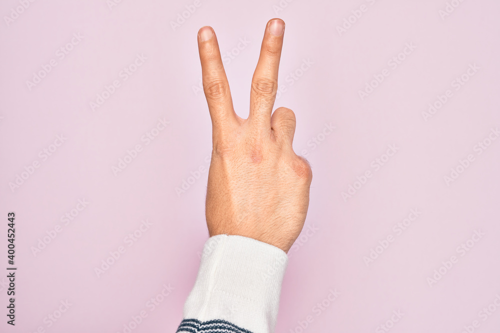 Hand of caucasian young man showing fingers over isolated pink background counting number 2 showing two fingers, gesturing victory and winner symbol Hand of caucasian young man showing fingers over isolated pink background counting number 2 showing two fingers, gesturing victory and winner symbol