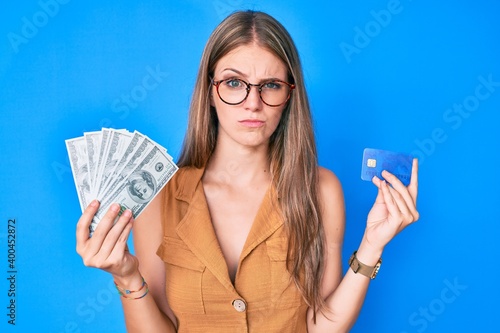 Young blonde girl holding credit car and dollars skeptic and nervous, frowning upset because of problem. negative person.