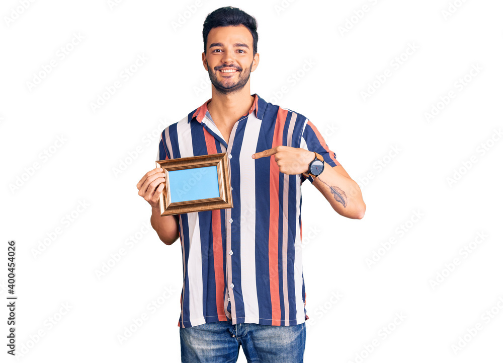 Young handsome hispanic man holding empty frame smiling happy pointing with hand and finger Young handsome hispanic man holding empty frame smiling happy pointing with hand and finger