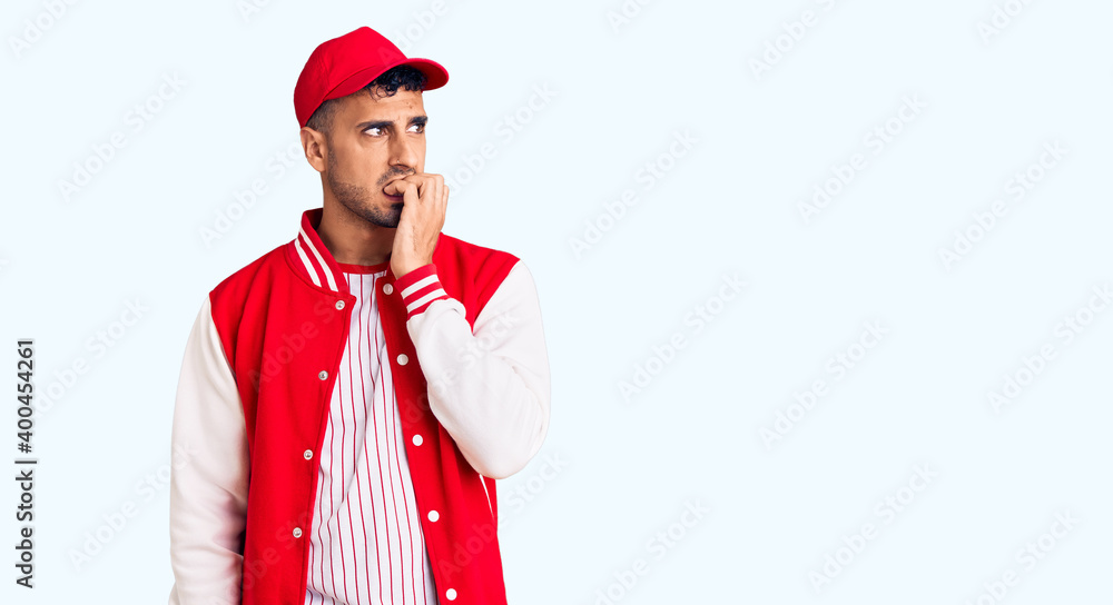 Young hispanic man wearing baseball uniform looking stressed and nervous with hands on mouth biting nails. anxiety problem. Young hispanic man wearing baseball uniform looking stressed and nervous with hands on mouth biting nails. anxiety problem.