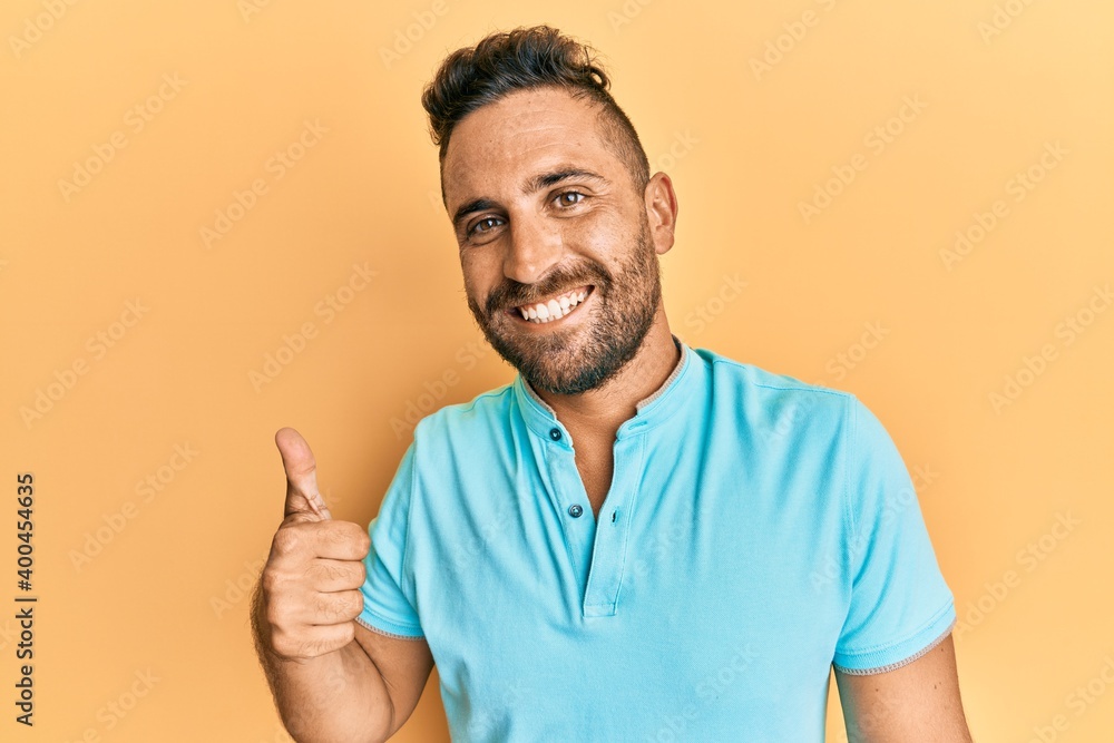 Handsome man with beard wearing casual clothes smiling happy and positive, thumb up doing excellent and approval sign Handsome man with beard wearing casual clothes smiling happy and positive, thumb up doing excellent and approval sign