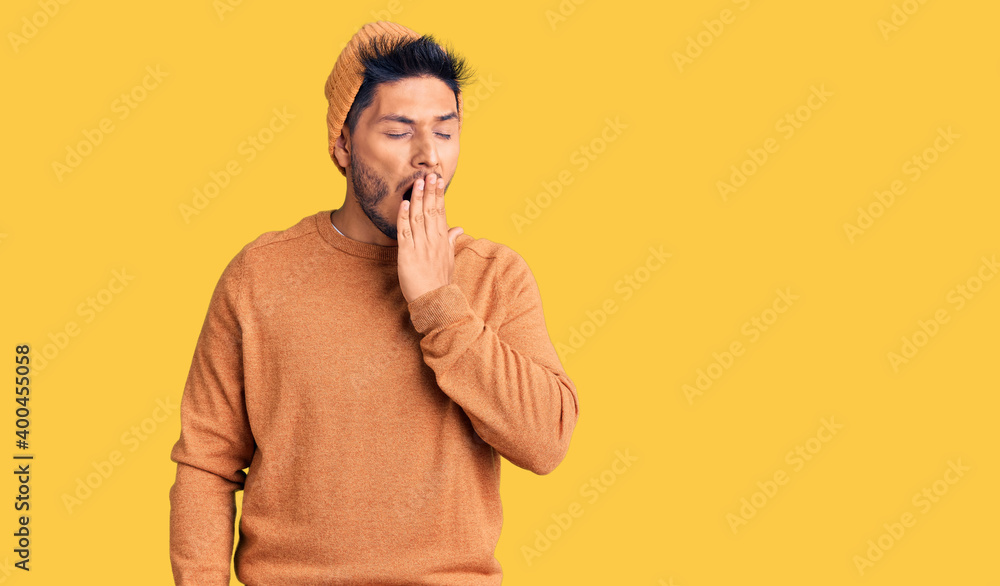 Handsome latin american young man wearing winter sweater and wool hat bored yawning tired covering mouth with hand. restless and sleepiness. Handsome latin american young man wearing winter sweater and wool hat bored yawning tired covering mouth with hand. restless and sleepiness.