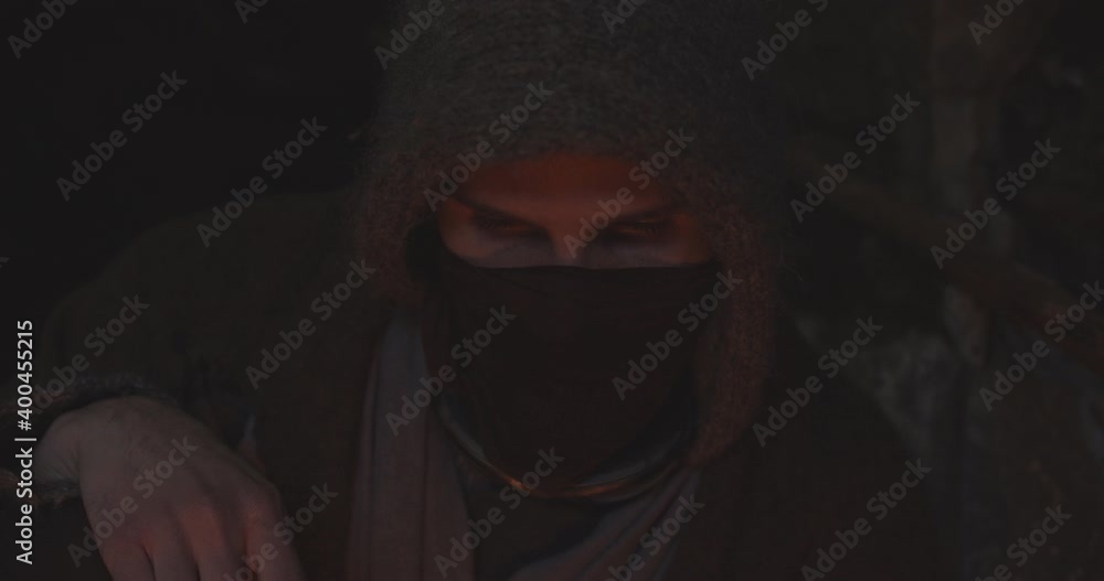 Hooded And Masked Figure In Cave Staring Fire Hooded And Masked Figure In Cave Staring Fire