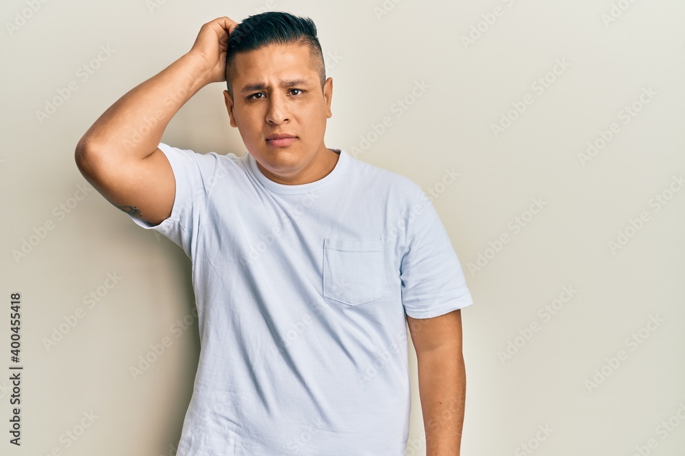 Young latin man wearing casual white t shirt confuse and wonder about question. uncertain with doubt, thinking with hand on head. pensive concept. Young latin man wearing casual white t shirt confuse and wonder about question. uncertain with doubt, thinking with hand on head. pensive concept.