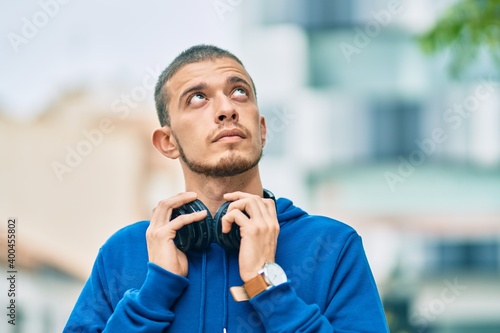 Young hispanic man with serious expression using headphones at the city