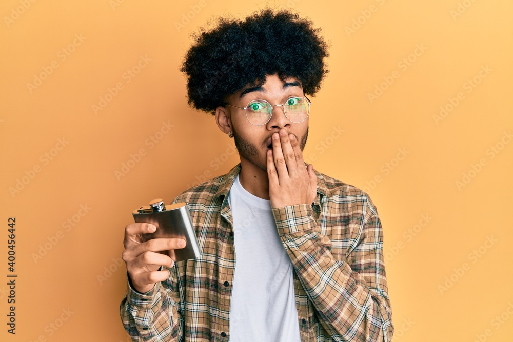 Young african american man with afro hair drinking alcohol from whiskey flask covering mouth with hand, shocked and afraid for mistake. surprised expression Young african american man with afro hair drinking alcohol from whiskey flask covering mouth with hand, shocked and afraid for mistake. surprised expression