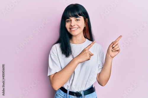 Young hispanic girl wearing casual clothes smiling and looking at the camera pointing with two hands and fingers to the side.