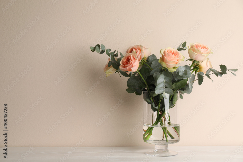 Naklejka premium Vase with bouquet of beautiful roses on white wooden table. Space for text