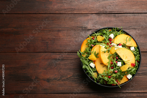 Delicious persimmon salad with pomegranate and arugula on wooden table, top view. Space for text