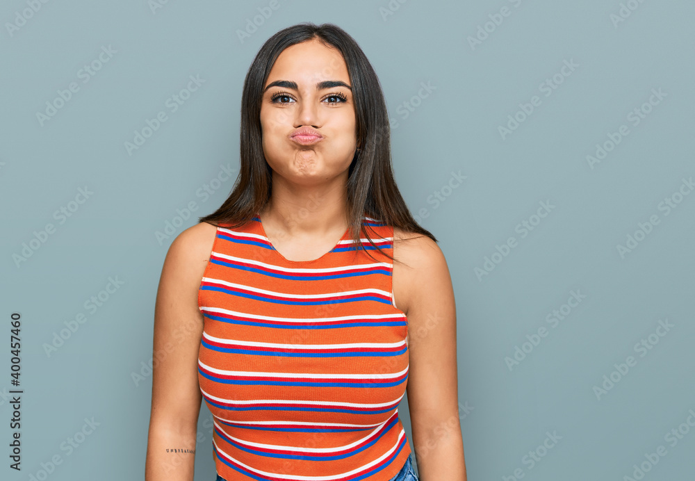 Obraz premium Young brunette woman wearing casual clothes puffing cheeks with funny face. mouth inflated with air, crazy expression.