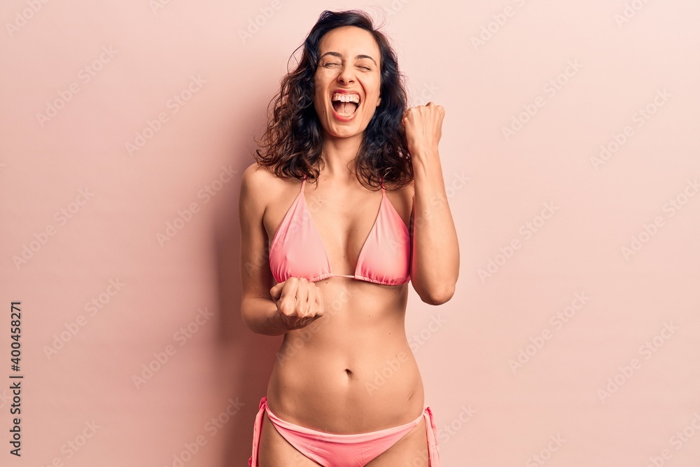 Young beautiful hispanic woman wearing bikini celebrating surprised and amazed for success with arms raised and eyes closed Young beautiful hispanic woman wearing bikini celebrating surprised and amazed for success with arms raised and eyes closed