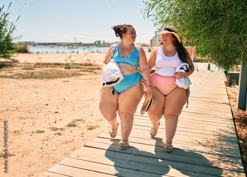 Photography Two plus size overweight sisters twins women walking at the beach on summer holi