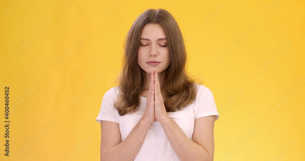 Young peaceful woman praying to God, clasping hands and closing her eyes during meditation, orange studio background Young peaceful woman praying to God, clasping hands and closing her eyes during meditation, orange studio background