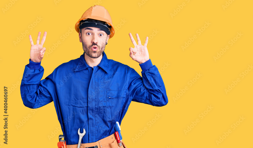 Young hispanic man wearing worker uniform looking surprised and shocked doing ok approval symbol with fingers. crazy expression