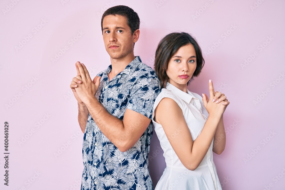Beautiful couple wearing casual clothes holding symbolic gun with hand gesture, playing killing shooting weapons, angry face Beautiful couple wearing casual clothes holding symbolic gun with hand gesture, playing killing shooting weapons, angry face