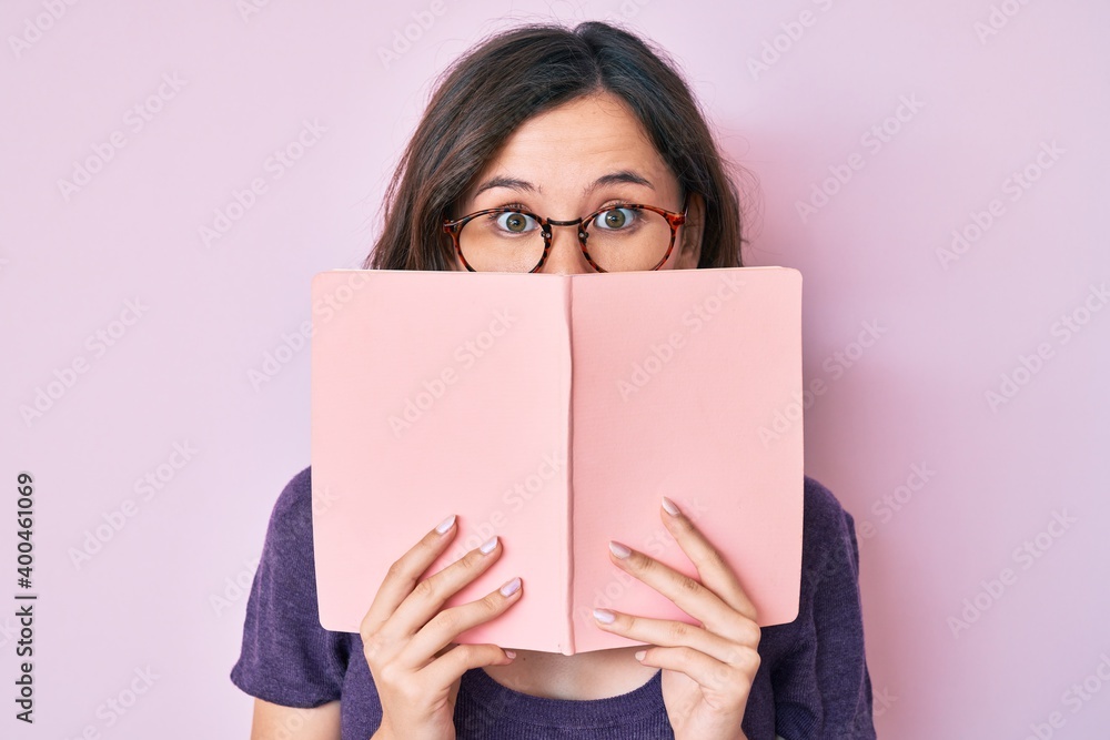 Young beautiful woman wearing glasses reading book puffing cheeks with funny face. mouth inflated with air, catching air. Young beautiful woman wearing glasses reading book puffing cheeks with funny face. mouth inflated with air, catching air.