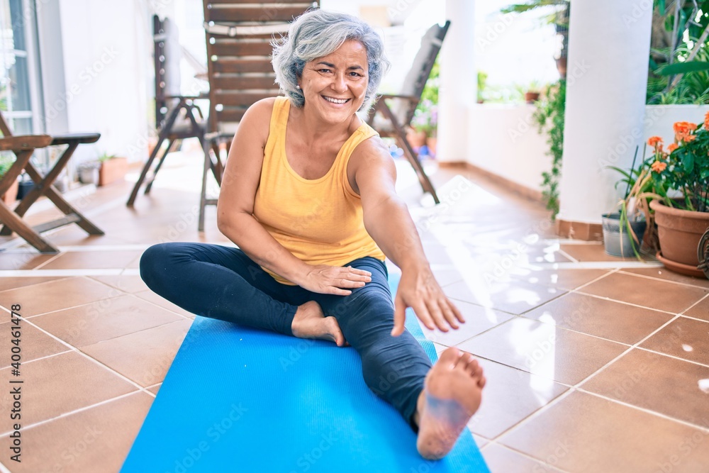 Fototapeta premium Middle age woman with grey hair smiling happy doing exercise and stretching on the terrace at home
