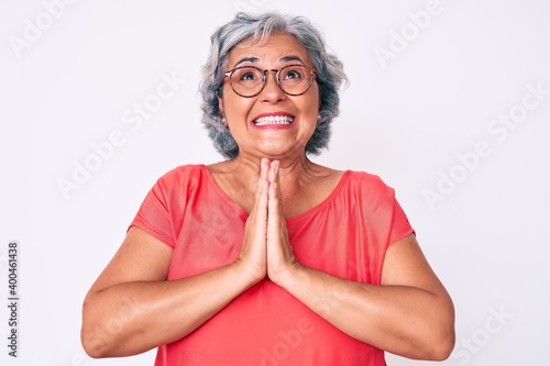 Senior hispanic grey- haired woman wearing casual clothes and glasses begging and praying with hands together with hope expression on face very emotional and worried. begging.