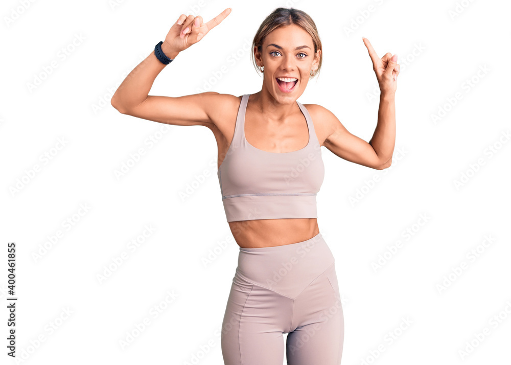 Beautiful caucasian woman wearing sportswear smiling amazed and surprised and pointing up with fingers and raised arms. Beautiful caucasian woman wearing sportswear smiling amazed and surprised and pointing up with fingers and raised arms.