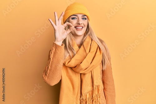 Young caucasian woman wearing wool winter sweater and cap smiling positive doing ok sign with hand and fingers. successful expression.