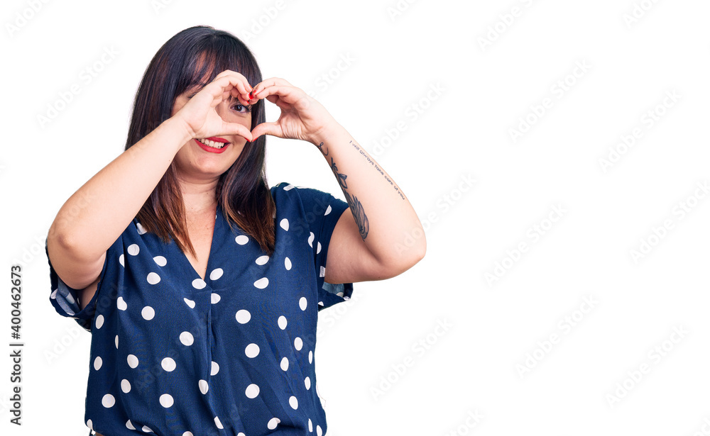 Young plus size woman wearing casual clothes doing heart shape with hand and fingers smiling looking through sign Young plus size woman wearing casual clothes doing heart shape with hand and fingers smiling looking through sign