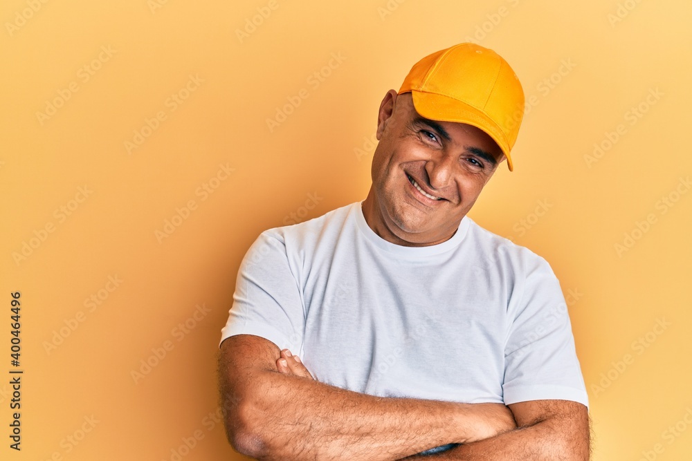Mature middle east man with mustache wearing casual white tshirt and yellow cap happy face smiling with crossed arms looking at the camera. positive person. Mature middle east man with mustache wearing casual white tshirt and yellow cap happy face smiling with crossed arms looking at the camera. positive person.
