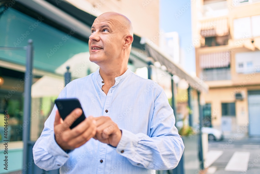 Fototapeta premium Middle age bald man smiling happy using smartphone at the city.