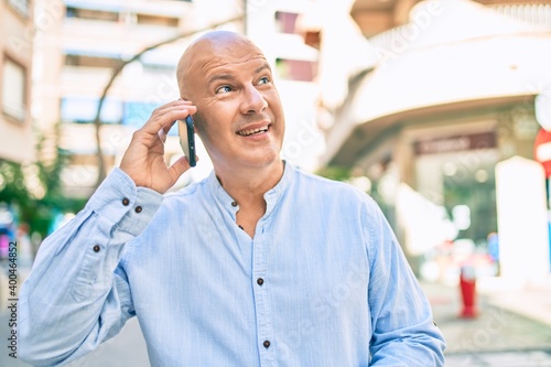 Middle age bald man smiling happy talking on the smartphone at the city.