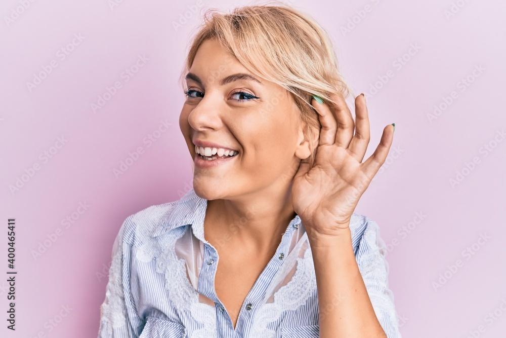 Young blonde girl wearing casual clothes smiling with hand over ear listening an hearing to rumor or gossip. deafness concept. Young blonde girl wearing casual clothes smiling with hand over ear listening an hearing to rumor or gossip. deafness concept.