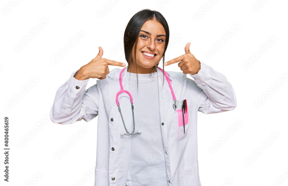 Beautiful hispanic woman wearing doctor uniform and stethoscope smiling cheerful showing and pointing with fingers teeth and mouth. dental health concept. Beautiful hispanic woman wearing doctor uniform and stethoscope smiling cheerful showing and pointing with fingers teeth and mouth. dental health concept.