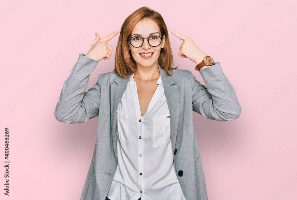 Young caucasian woman wearing business style and glasses smiling pointing to head with both hands finger, great idea or thought, good memory Young caucasian woman wearing business style and glasses smiling pointing to head with both hands finger, great idea or thought, good memory
