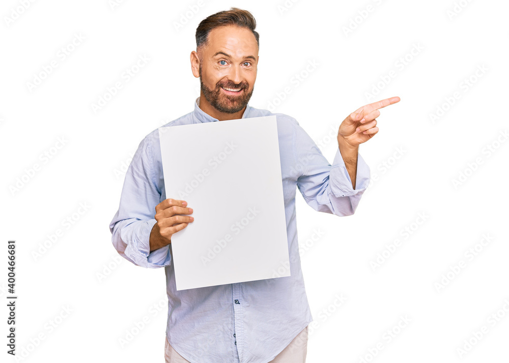 Handsome middle age man holding blank empty banner smiling happy pointing with hand and finger to the side Handsome middle age man holding blank empty banner smiling happy pointing with hand and finger to the side