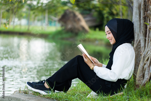 A beautiful Islamic woman sitting by the pond reading a book.