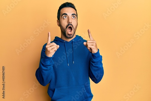Young hispanic man wearing casual clothes amazed and surprised looking up and pointing with fingers and raised arms.