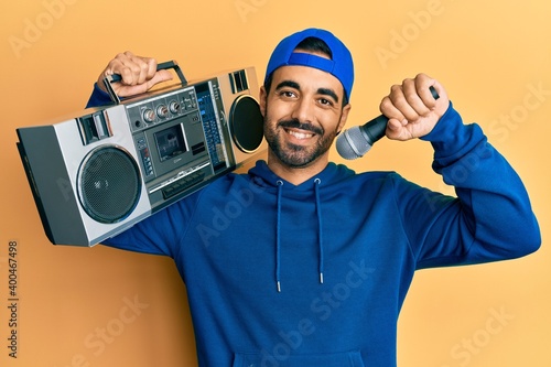 Young hispanic man holding boombox, listening to music singing with microphone smiling with a happy and cool smile on face. showing teeth.