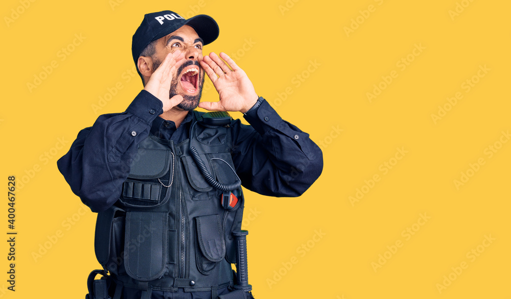 Young hispanic man wearing police uniform shouting angry out loud with hands over mouth Young hispanic man wearing police uniform shouting angry out loud with hands over mouth