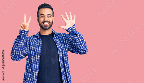 Young hispanic man wearing casual clothes showing and pointing up with fingers number seven while smiling confident and happy.